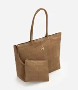Cartera amplia confeccionada en fibra de papel, de color beige, con asas de hombro, cierre superior y detalle metálico dorado claro en el frente.