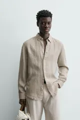 Camisa de manga larga color beige claro, confeccionada en lino, con cuello italiano y cierre frontal de botonadura.