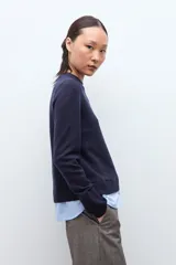Sweater azul marino de manga larga con cuello redondo, combinado con una camisa celeste que se asoma por debajo.
