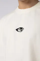 Remera de corte oversize confeccionada en algodón pesado, color negro. Presenta un bordado minimalista en el centro del pecho con forma de ojo y un parche estampado en la espalda que ilustra una mano abriendo una persiana.