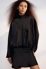 Vestido corto negro de tejido satinado, con cuello alto, mangas largas amplias y detalle de frunces en la cintura.