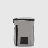 Bolso tipo crossbag color gris, de diseño minimalista y funcional. Cuenta con cierre superior impermeable, compartimento principal con cierre, bolsillo trasero magnético y parche frontal con logo. Incluye correa ajustable para llevar al frente o en la espalda.