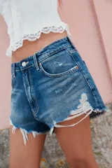 Shorts de jean de tiro alto con diseño curvo, cinco bolsillos y trabillas para cinturón. Presenta roturas desgastadas y bajo con acabado deshilachado. Cierre frontal con cremallera y botón metálico.