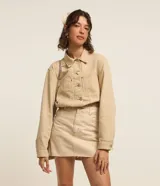 Campera color beige confeccionada en sarga de algodón, de corte regular, con cuello camisero, cierre abotonado, manga larga, bolsillos frontales y recortes.