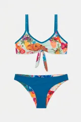 Conjunto de bikini de dos piezas con estampado floral en tonos rojo, violeta y verde sobre fondo claro, con detalles en color amarillo en los bordes y tirantes. El corpiño es de estilo deportivo con tiras para anudar al frente, y la bombacha es de corte clásico.