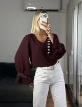 Blusa de tela cey color bordó, con escote en V y mangas largas abullonadas que terminan en puños con detalle de encaje y volados.