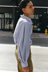 Camisa de manga larga con cuello solapa, cierre frontal con botones y bajo asimétrico, con estampado de rayas verticales.