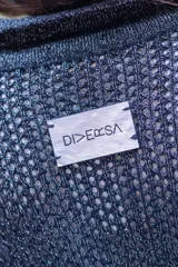 Camisa tejida en punto calado color marrón con hilo de algodón y lurex. Silueta oversize, mangas 3/4 ligeramente abullonadas, cuello camisero clásico y botonadura frontal con botones metálicos dorados.