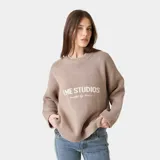 Suéter de punto grueso color marrón topo, con corte relajado y ligeramente corto. Presenta cuello redondo y puños acanalados, con el logo de la marca y la frase 'curated by ben ice' en jacquard blanco en el frente.