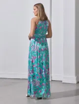 Vestido largo de gasa con estampado floral en tonos turquesa, rosa y verde. Tiene cuello halter cruzado, corte en la cintura con faja plisada y abertura en la espalda con cierre invisible.