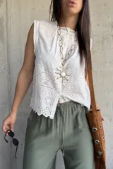 Camisa sin mangas blanca de broderie, con cuello alto fruncido y cierre frontal con botones.