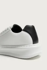 Zapatilla deportiva de diseño minimalista, confeccionada en material sintético negro con suela de plataforma blanca y detalle de contraste en el talón.