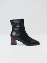 Botas de cuero color marrón con caña media y punta cuadrada. Presentan un cierre trasero, tirador para calzar fácilmente y bordado en color contrastante en el empeine. Suela de goma y taco de madera de 6 cm de altura.