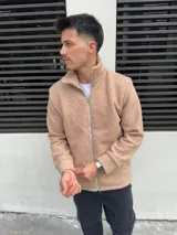Campera de corderito color beige con cierre frontal completo y cuello alto. Presenta puños y ruedo acanalados, con detalles de terminación en tela lisa a lo largo del cierre.