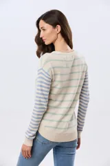Buzo tejido de algodón con diseño a rayas horizontales, cuello redondo y mangas largas. El cuerpo presenta rayas en tonos azul y beige, mientras que las mangas combinan rayas en tonos azul y rosado.