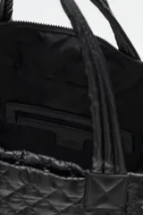 Bolso tote grande acolchado color vino tinto, con costuras en patrón de rombos. Posee dos asas de mano y una correa ajustable y desmontable con texto repetido. Incluye un charm colgante con letras negras.