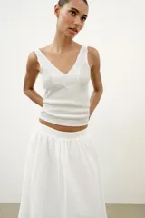 Top de punto canalé en color beige, con escote en pico adornado con una delicada aplicación de encaje blanco y tirantes anchos.