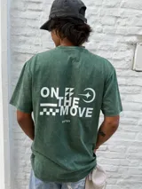 Remera de algodón color verde oscuro con efecto gastado (acid wash). Presenta un estampado minimalista en el pecho con el texto "ON THE MOVE" y un patrón de cuadros blancos a la derecha.