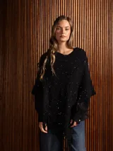 Poncho tejido asimétrico de color negro, con detalle de lentejuelas sutiles distribuidas por toda la prenda y terminación con flecos en el ruedo.