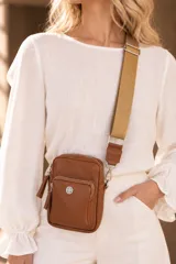 Bandolera pocket bag de cuero vacuno color suela, con bolsillo frontal con cierre y detalle de placa metálica con logo. Cuenta con correa de cinta ancha regulable y herrajes metálicos plateados.