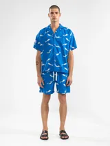 Camisa celeste con estampado de sirenas blancas, de corte recto con cuello camisero y mangas cortas.