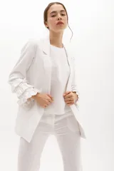 Blazer blanco de lino con solapas, cierre de un botón y mangas largas con volantes en capas.
