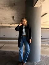 Camisa larga negra con cuello clásico, cierre frontal con botones a presión, mangas largas con puños de cuero y bolsillos de cuero con pespuntes blancos.