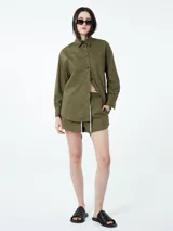Conjunto de dos piezas compuesto por una camisa de manga larga con cuello clásico y cierre frontal de botones, y un short con cintura elástica y cordón ajustable. Ambas prendas son de color verde militar.