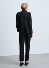 Pantalón de traje negro de tiro medio, con diseño recto y trabillas para cinturón. Cuenta con bolsillos laterales y dos bolsillos de ribete en la parte posterior, además de dobladillo vuelto en los tobillos.
