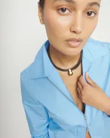 Collar de cuero negro con múltiples tiras y un colgante de bola grande de aleación de metales bañada en oro 18K. Cierre de mosquetón dorado con cadena de extensión.