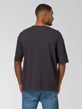 Remera de algodón con cuello redondo y manga corta, color negro con efecto desgastado. Presenta un pequeño bordado con el logo de la marca en el centro del pecho y un parche tejido en la manga.