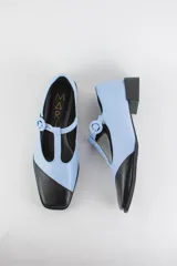 Zapatos de tacón bajo estilo Mary Jane, confeccionados 100% en cuero, con diseño bicolor en celeste y puntera diagonal en negro. Cuentan con tira en T y hebilla circular ajustable en el empeine, punta cuadrada y taco bajo cuadrado.