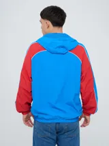 Campera deportiva Umbro del Club Nacional de Football, modelo Venti, para hombre. Diseño en color blanco con mangas azules y detalles de líneas rojas. Cuenta con capucha con cordón ajustable, cierre frontal y bolsillos. Presenta el logo de Umbro y el escudo del club bordados en el pecho.