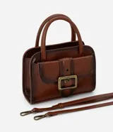 Cartera pequeña de mano con diseño estructurado, confeccionada en poliuretano color marrón con acabado envejecido. Cuenta con tapa frontal decorada con una hebilla metálica, cierre principal con cremallera, asa de mano rígida y correa larga ajustable y desmontable.