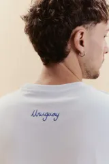 Remera de manga corta celeste con bordado en la parte posterior superior que dice 'Uruguay' en letra cursiva azul.