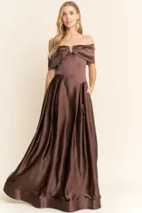 Vestido largo de fiesta confeccionado en satén color marrón chocolate. Presenta un diseño strapless con escote tipo solapa que cae sobre los hombros, cuerpo entallado y falda amplia con vuelo y bolsillos laterales.