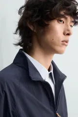 Chaqueta de corte relajado, color azul marino oscuro, confeccionada en tejido técnico ligero. Presenta cuello subido, forro interior de malla, bolsillos de vivo en cadera y bajo ajustable con elástico lateral. Cierre frontal con cremallera de doble dirección.