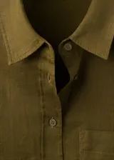Camisa de lino color verde militar, de corte recto con cuello camisero, manga larga con puños abotonados, bolsillo de parche en el pecho y cierre frontal de botones.