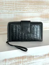 Billetera grande color negro con textura símil cuero de cocodrilo, cierre perimetral con cremallera y correa de muñeca extraíble.