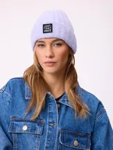 Gorro tipo beanie de punto acanalado en color lila, con parche rectangular negro en el frente que incluye la inscripción 'EAT THE WAVE'.