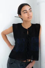 Chaleco de punto calado celeste con diseño estampado en negro y cierre frontal mediante tiras tejidas a crochet.
