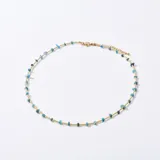 Gargantilla dorada con pequeñas cuentas doradas y piedras irregulares de color celeste.