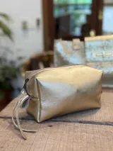Neceser de cuero con acabado metalizado dorado, cierre superior con tirador de cuero y diseño rectangular estructurado.