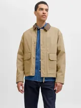 Campera utility de manga larga color beige, con cuello camisero de pana marrón. Tiene cierre de botones, dos bolsillos frontales con solapa y un interior forrado en poliéster reciclado. Cuenta con acabado repelente al agua.