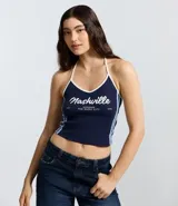 Top frente única de algodón en color azul marino con ribetes blancos en el cuello y rayas laterales. Presenta un estampado frontal con la inscripción Nashville y detalles en blanco. Diseño sin mangas con lazo para anudar al cuello.