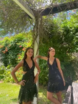 Vestido corto negro con estampado de plumas doradas, escote en V, breteles finos cruzados en la espalda, cut-outs laterales y volado en el ruedo.