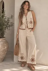 Conjunto de dos piezas compuesto por una musculosa y un short. La musculosa es sin mangas, con escote en V, cierre frontal con tiras para anudar y detalles bordados con diseño floral. El short cuenta con cintura elástica. Las terminaciones de la prenda presentan bordes scalloped (ondulados) con detalles bordados en contraste.