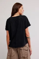 Remera henley de algodón liviano y jaspeado, de calce relajado, color blanco off-white, con mangas cortas, botonadura al cuello, aplicaciones de encaje y ruedo enrollado.