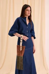 Bolso estilo bucket de cuero marrón, con flecos largos de gamuza verde oliva en la base y asa de mano tejida en macramé color natural.