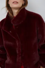 Chaqueta de piel sintética en color burdeos, con cuello alto y cierre frontal oculto. Presenta un diseño de corte recto y mangas largas con puños ligeramente ajustados.